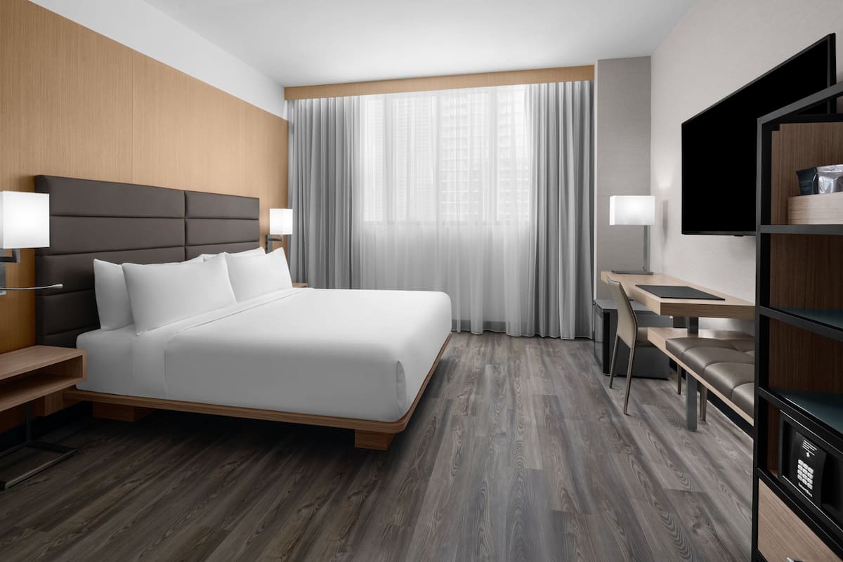 Ein modernes Hotelzimmer mit einem großen Bett, Nachttischen, einem Schreibtisch und einem Fernseher.