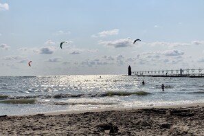 A beach with sand, waves, and a pier in the background.
