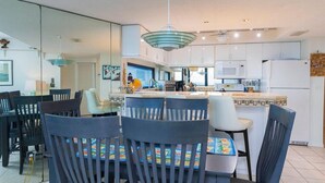 A modern kitchen with white cabinets, a central island, and a dining area with chairs and a table. - Anastasia Condos Oceanfront – Spectacular Views & Great Rates! (Saint Augustine)