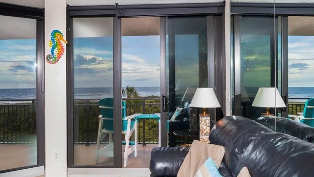 A modern living room with a black leather sofa, two lamps, and a view of the ocean through large glass doors. - Anastasia Condos Oceanfront – Spectacular Views & Great Rates! (Saint Augustine)