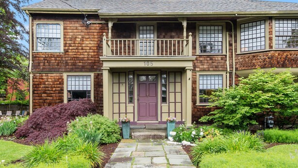 Une maison à deux étages avec un porche à l’avant, le numéro « 105 » au-dessus de la porte et un jardin bien entretenu.