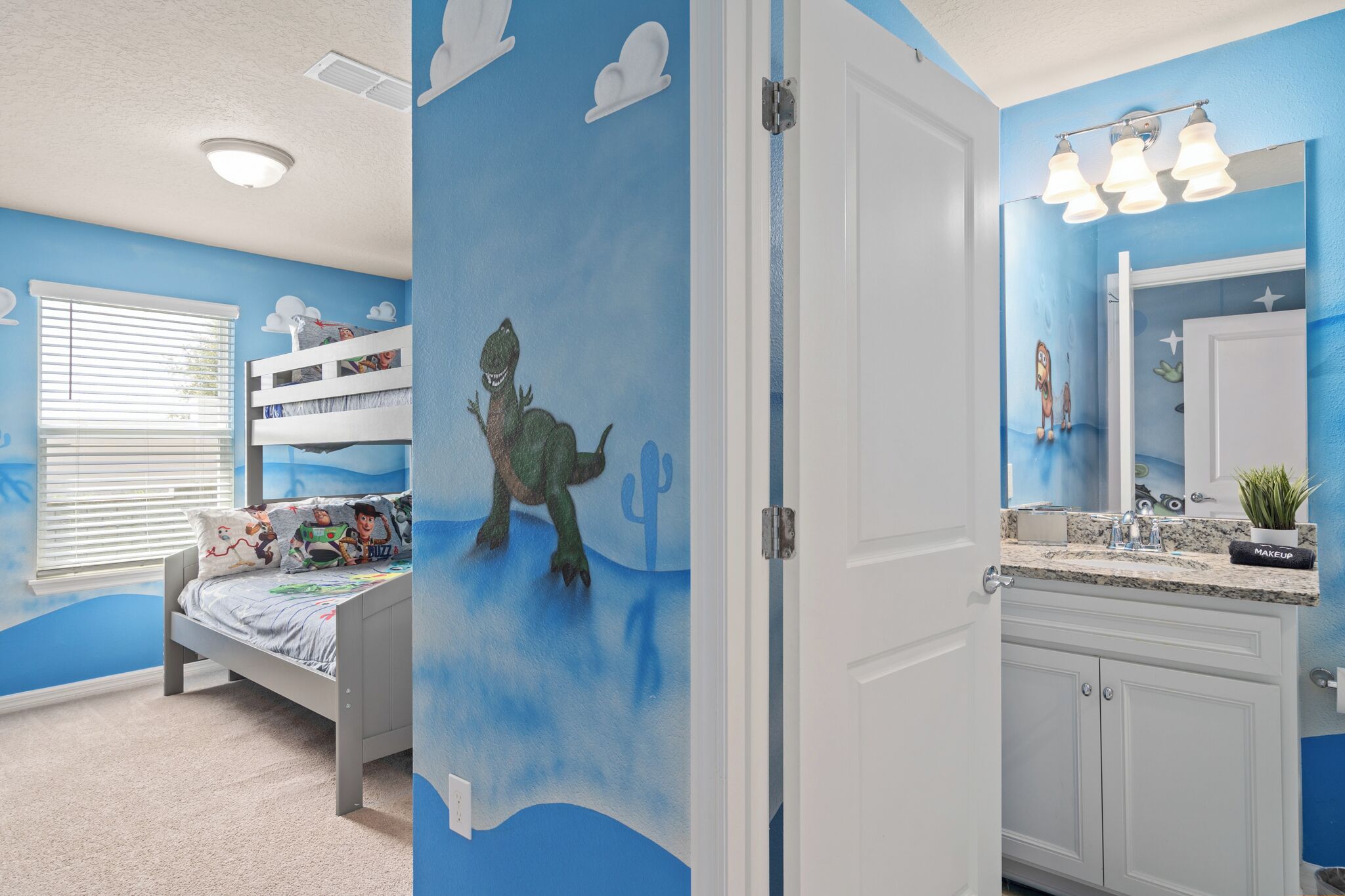 Ein Kinderzimmer mit Etagenbett, einer Wandmalerei eines Dinosauriers und einem Badezimmer mit Waschbecken und Waschtisch.
