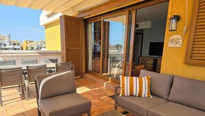 Une terrasse ensoleillée avec un canapé, des chaises et une table.