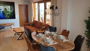 Un coin repas avec une table en bois dressée pour quatre personnes, entourée de chaises, d’un canapé et d’un grand tableau.