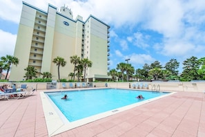 A hotel pool area with a large pool, lounge chairs, and palm trees.