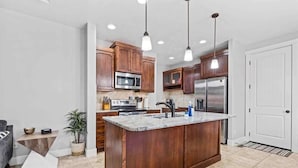 A modern kitchen with wooden cabinets, stainless steel appliances, and pendant lighting. - Stylish Meridian Retreat Near The Village | 3BR Family Stay w/ Patio (Meridian)