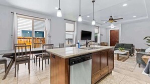 A modern kitchen with a central island, dining area, and a living space with a sofa and coffee table. - Stylish Meridian Retreat Near The Village | 3BR Family Stay w/ Patio (Meridian)