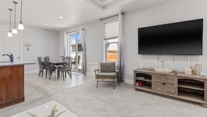 A modern living room with a dining area, a flat-screen TV mounted on the wall, and a wooden entertainment unit. - Stylish Meridian Retreat Near The Village | 3BR Family Stay w/ Patio (Meridian)