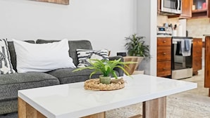 A modern living room with a white coffee table, grey sofa, and a kitchen area in the background. - Stylish Meridian Retreat Near The Village | 3BR Family Stay w/ Patio (Meridian)