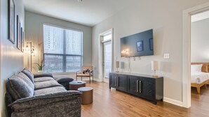 A modern living room with a gray sofa, a round coffee table, a dark wooden cabinet, and a flat-screen TV mounted on the wall.