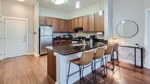 A modern kitchen with wooden cabinets, a central island with bar stools, a refrigerator, and a microwave.