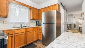 A modern kitchen with wooden cabinets, a stainless steel refrigerator, and a marble countertop. - Downtown Caldwell | Golf Course View | Near I-84 | Fast WiFi | Sleeps 5 (Caldwell)