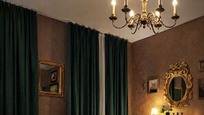 Un dormitorio con cama, cortinas verdes, candelabro, cómoda y espejo.