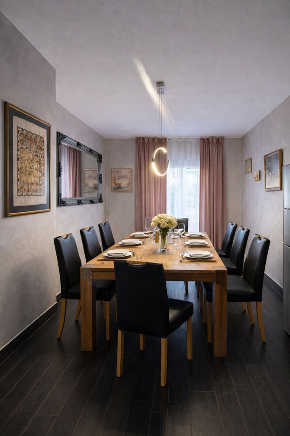 Un comedor con mesa de madera, sillas negras, un jarrón de flores y cuadros en las paredes.