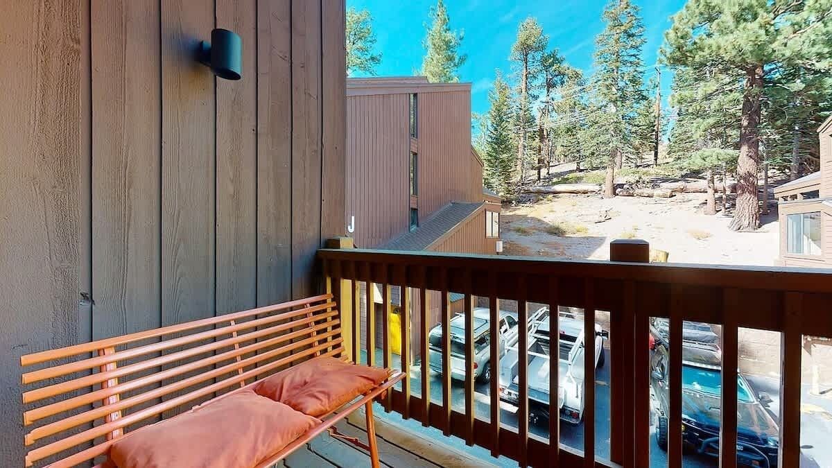 Eine Holzterrasse mit einer Bank, einem Geländer und Blick auf einen Wald sowie geparkte Autos.