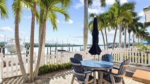 A patio with a table and chairs, a white picket fence, and palm trees. - Waterfront 1/1, sleeps 6, walk to beach! #B111 (Indian Shores)