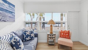 A room with a sofa, a chair, a lamp, and a view through large windows. - Waterfront 1/1, sleeps 6, walk to beach! #B111 (Indian Shores)