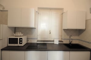 A compact kitchen with white cabinets, a microwave, a sink, and a tiled backsplash. - La Piazzetta by Amalfidreams (MINORI)