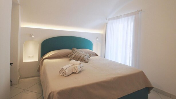 A neatly made bed with a teal headboard, a beige bedspread, and a rolled towel on the side. - La Piazzetta by Amalfidreams (MINORI)