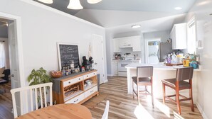 Ett modernt kök med vita skåp, ett matbord i trä och en menytavla i form av en svart tavla.
