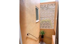 Ein kleiner, abgeschlossener Außenbereich mit strukturierter Wand, einem Fenster, einem Blumentopf und einem dekorativen Gitter.