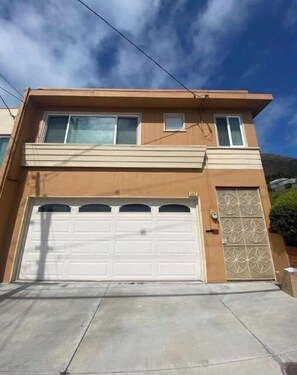 Two-story residential building with a flat roof and symmetrical facade, featuring a large garage door and a balcony with a small window.