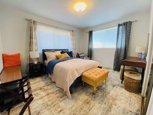 A bedroom with a bed, bedside table, chair, and a small desk with a lamp.