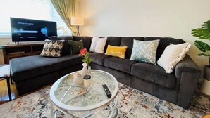 Ein Wohnzimmer mit einem dunkelgrauen Sofa, einem Glastisch und einem Fernseher, der 'Verbindung herstellen' anzeigt.