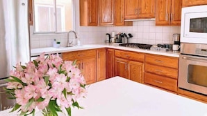Eine Küche mit Holzausstattung, einer weißen Arbeitsplatte, einem Edelstahlkühlschrank, einer Mikrowelle und einer Vase mit rosa Blumen.