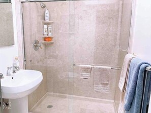 A modern bathroom with a glass-enclosed shower, a sink, and a towel rack with towels.