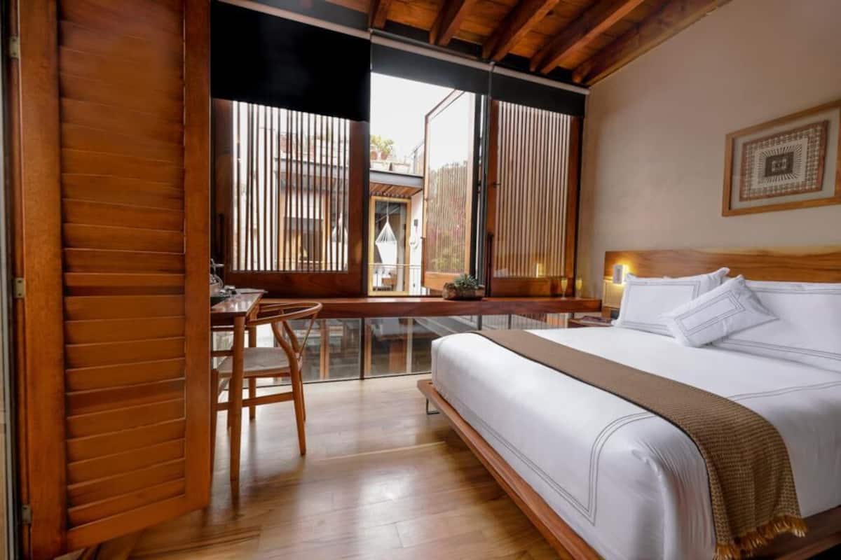 Un dormitorio con una cama grande, suelo de madera, un escritorio y vistas al exterior.