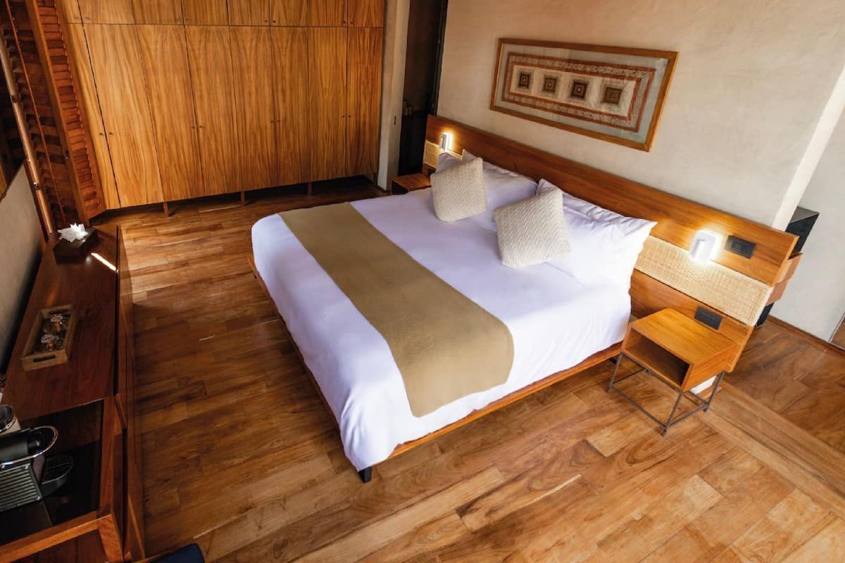 Habitación de hotel con una cama grande, armario de madera, mesitas de noche y un cuadro enmarcado en la pared.