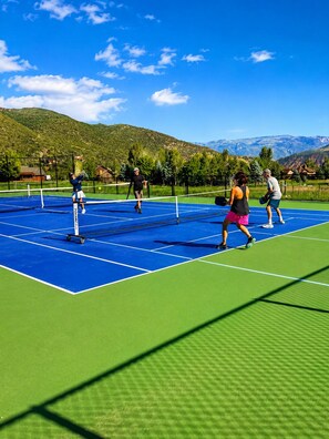A tennis court with a net, surrounded by greenery and mountains.