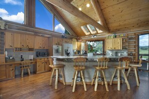 Eine geräumige Küche mit Holzausstattung, einer zentralen Kochinsel mit Barhocker und großen Fenstern mit Blick ins Freie.