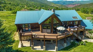 A log cabin with a blue metal roof, a deck with outdoor furniture, and a stone foundation.