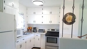 A kitchen with white cabinets, a refrigerator, a microwave, a coffee maker, and an oven.