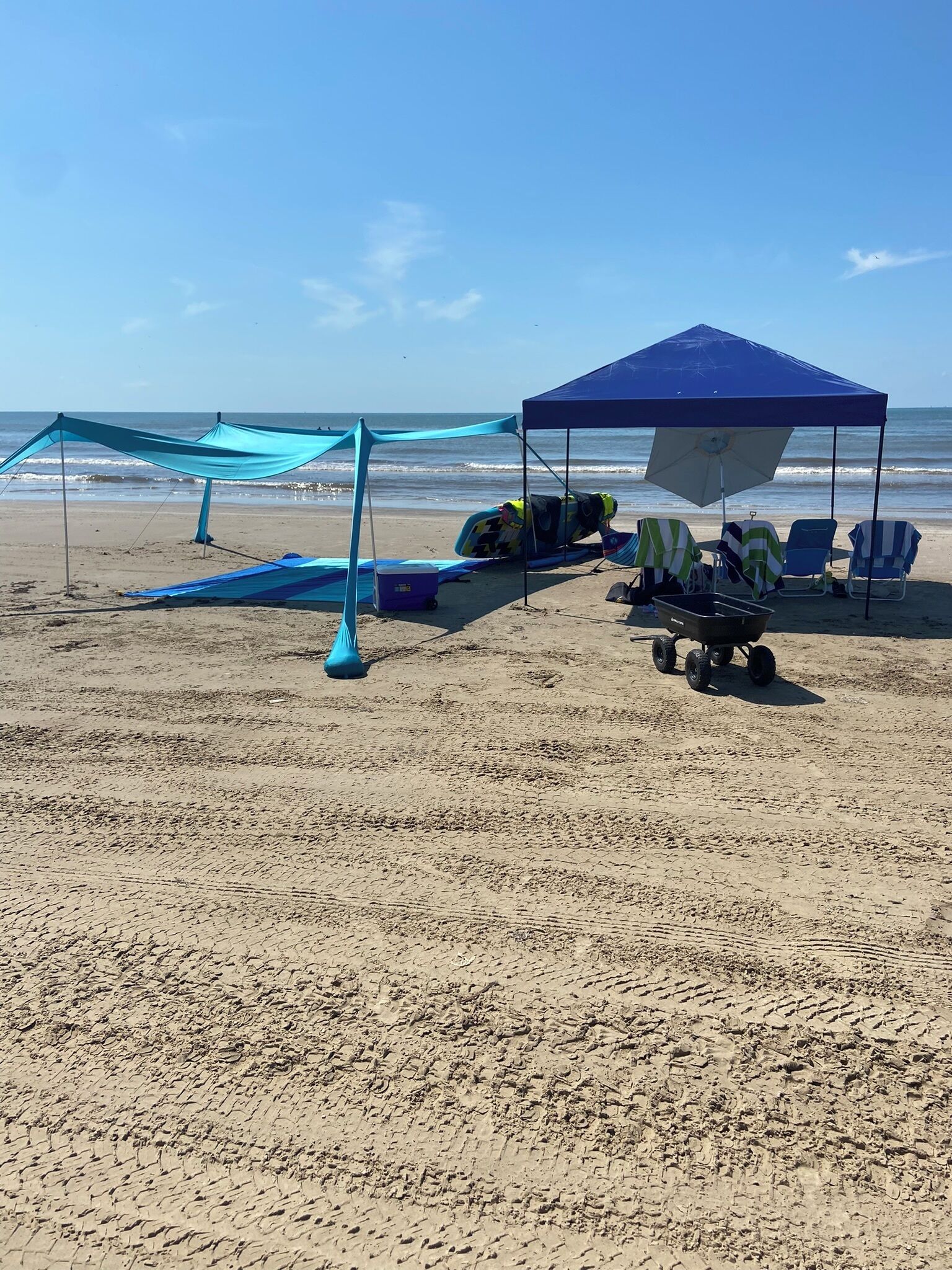 Une plage avec une tente bleue, des chaises de plage et un chariot de plage.