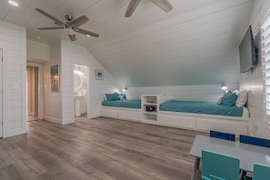 A bedroom with two beds, a ceiling fan, and a desk with chairs.