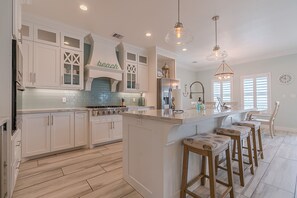 A kitchen with white cabinetry, a central island with stools, a stove, and pendant lighting.