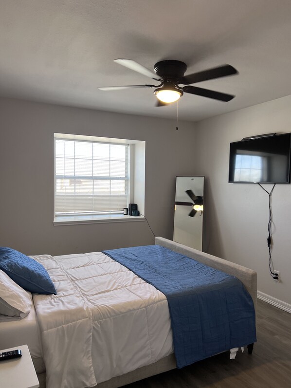 A bedroom with a bed, a ceiling fan, a TV, and a window with blinds.