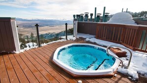 Un bain à remous sur une terrasse en bois, avec un paysage enneigé en arrière-plan.