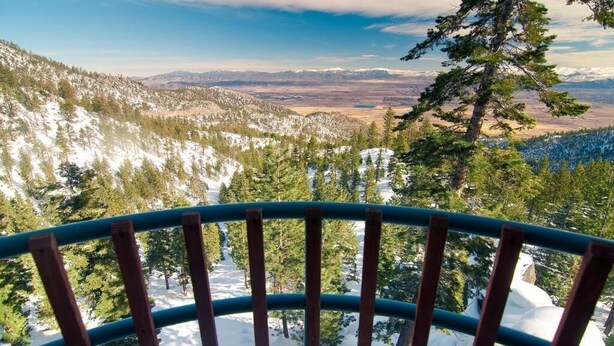 Un paysage montagneux enneigé offrant une vue dégagée sur des montagnes lointaines et une zone boisée.
