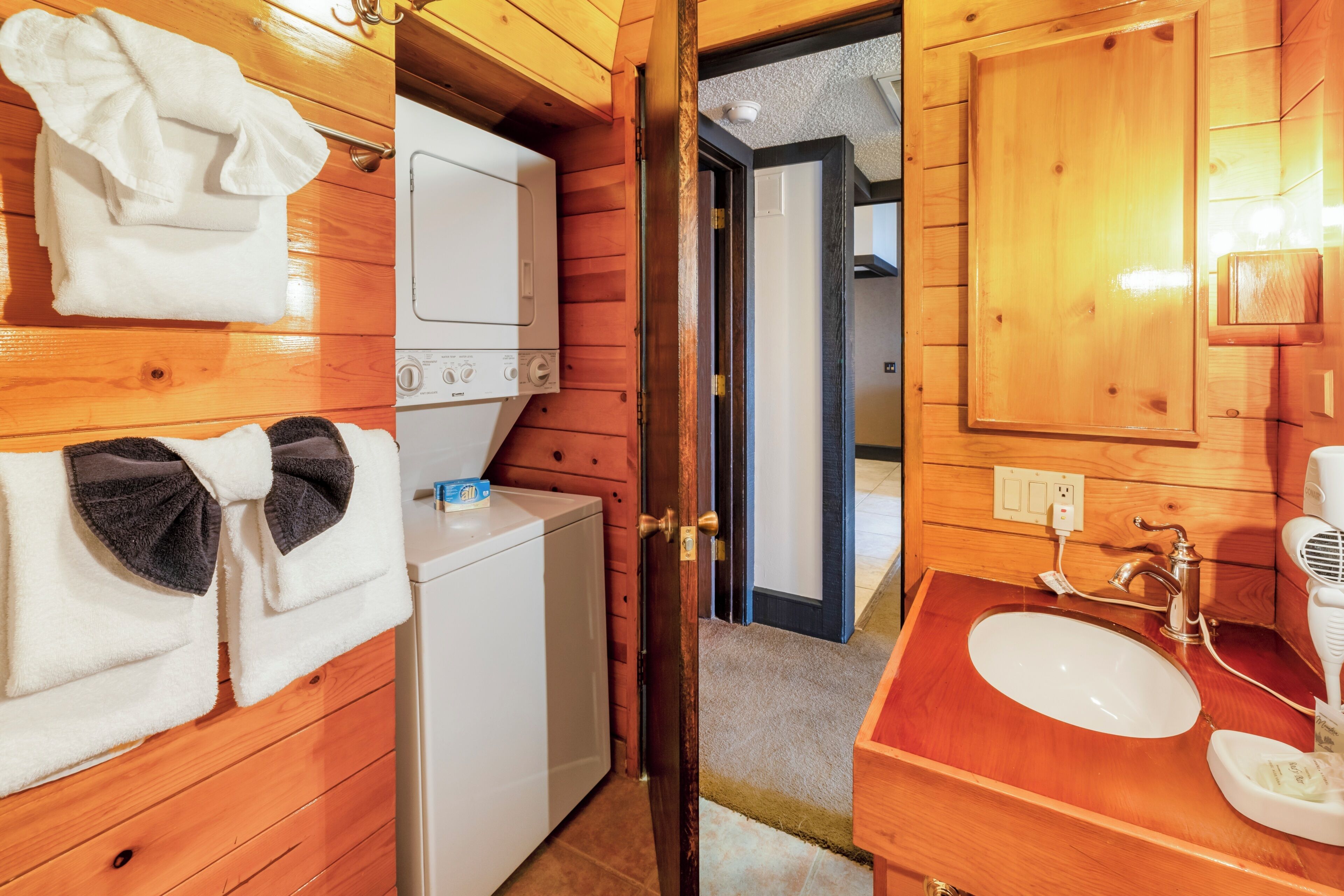 A wooden cabin interior with a washing machine, a sink with a mirror, and towels.