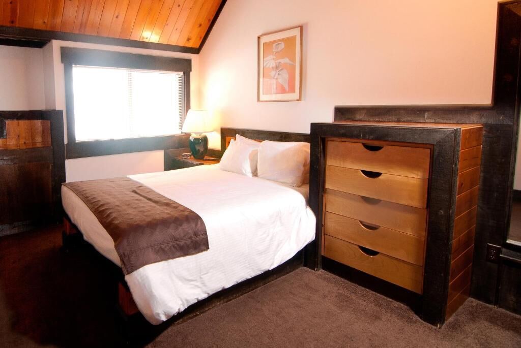 A bedroom with a bed, a nightstand, a dresser, a window, and a wall-mounted picture.