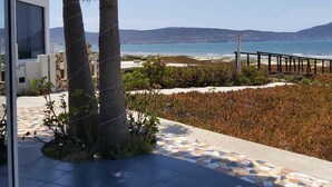 A terrace with palm trees, a tiled floor, and a view of the sea and distant hills.