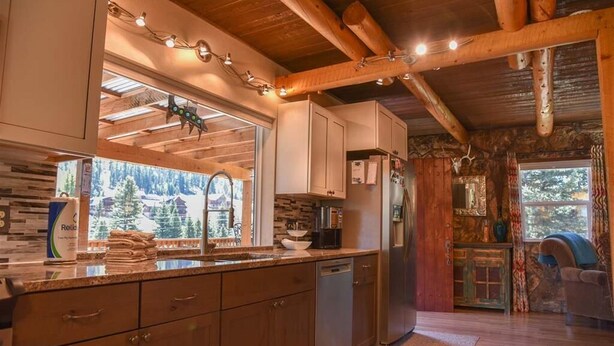 Une cuisine rustique avec des poutres en bois, une grande fenêtre et une vue sur la forêt.