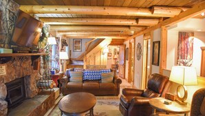 Un salon chaleureux avec une cheminée, des meubles en cuir et un escalier menant à l’étage supérieur.