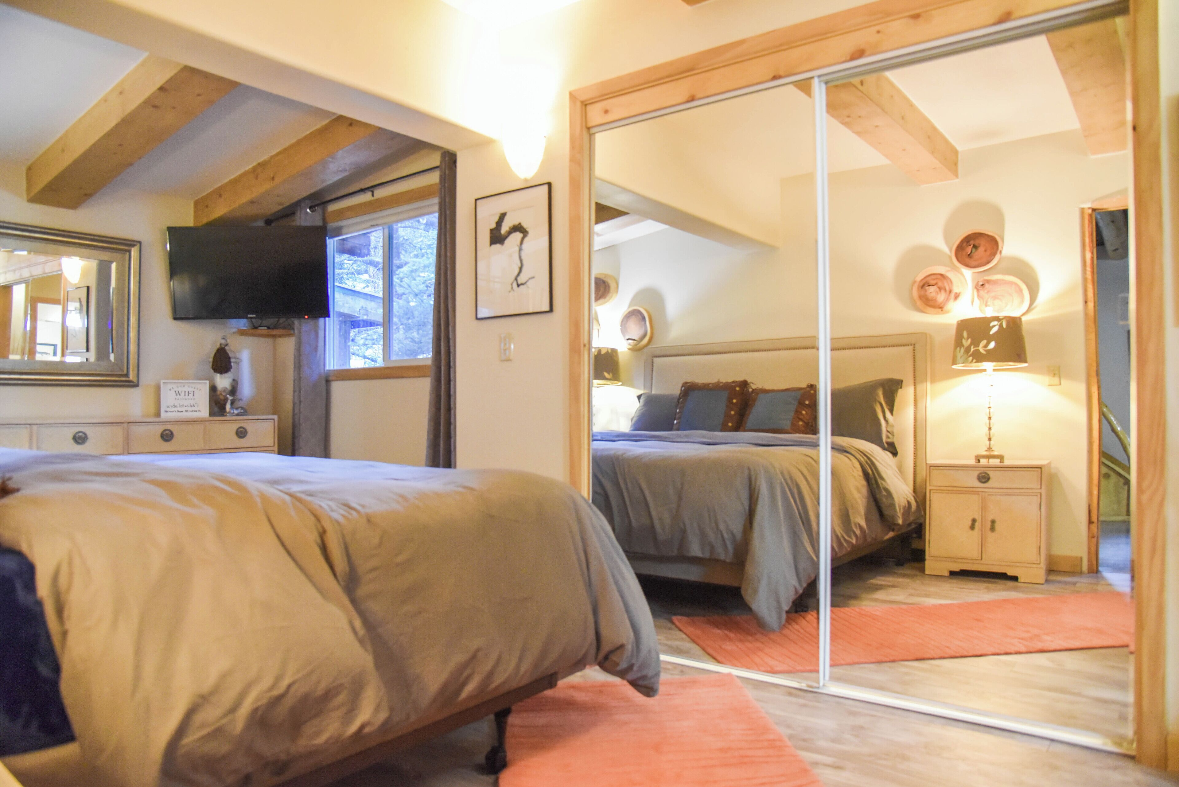 A bedroom with two beds, a TV, a mirror, and a small cabinet.