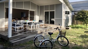 Un patio techado al aire libre con zona de comedor, una bicicleta y una terraza de madera.