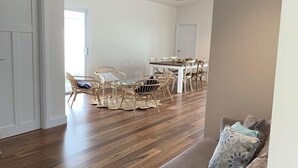 Un salón amplio con piso de madera, un sofá color beige y una mesa de comedor con sillas.